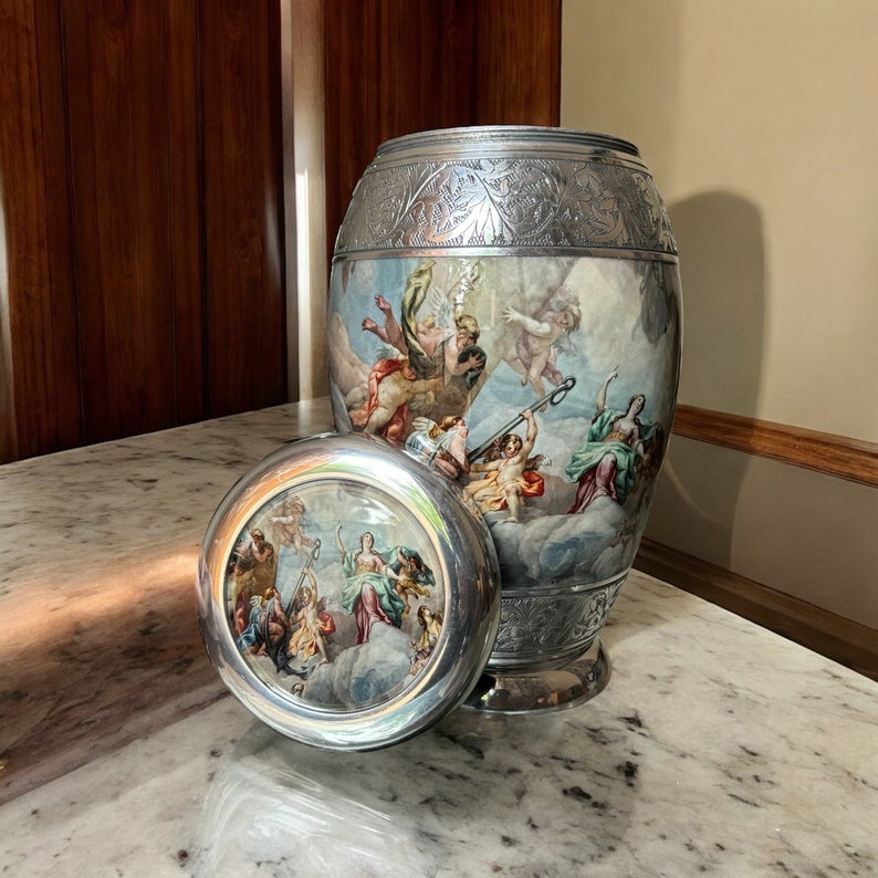 May include: A silver urn with an ornate design and a painted scene of figures in the clouds. The urn has a matching lid with a similar painted scene.