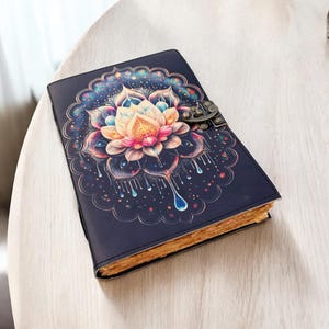 May include: A dark blue journal with a colorful lotus flower design on the cover. The floral design features shades of pink, orange, and blue. The journal has a metal clasp and aged-looking paper.
