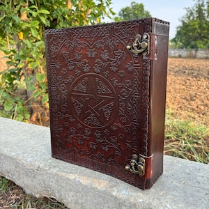 May include: A brown leather journal with a pentacle design and floral details. The journal has two brass clasps.