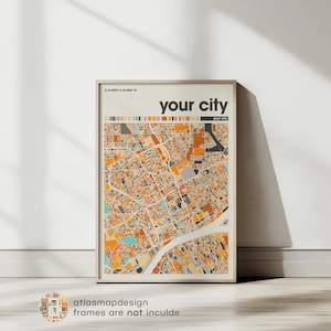 May include: A framed print of a city map, with the text "YOUR CITY" at the top. The map is an abstract design in various colours, with a river feature. The print is in a light-coloured frame and is propped against a white wall.