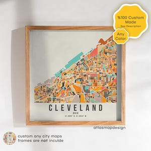 Puede incluir: Una impresión enmarcada del mapa de Cleveland, Ohio, con un diseño abstracto colorido en tonos naranja, turquesa y marrón. El nombre de la ciudad está en negrita, en negro, con las coordenadas debajo. El marco es de madera clara. El texto "custom any city maps" está en la parte inferior.