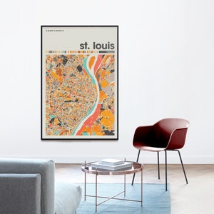 May include: A framed print of a colorful map of St. Louis, Missouri. The map is in a black frame and is hanging on a white wall. The map is surrounded by a light grey couch, a brown coffee table, and a red chair.