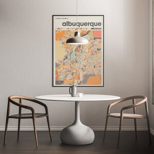 May include: A white round table with a gray pedestal base sits in a room with two wooden chairs. A black framed poster with the text "albuquerque new mexico" hangs on the wall behind the table. A light fixture hangs above the table.