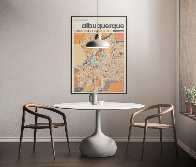 May include: A white round table with a gray pedestal base sits in a room with two wooden chairs. A black framed poster with the text "albuquerque new mexico" hangs on the wall behind the table. A light fixture hangs above the table.
