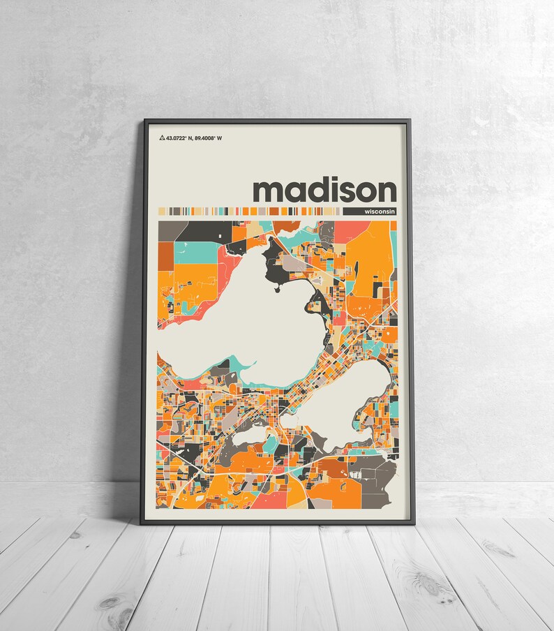 May include: A colorful map of Madison, Wisconsin, with the city name and coordinates in the top left corner. The map is in a black frame and is on a white wooden floor.