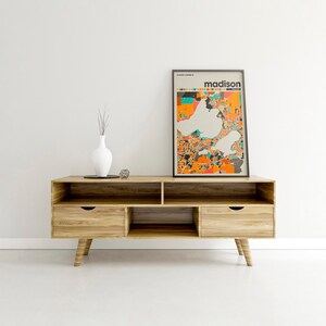 May include: A wooden entertainment center with two drawers and open shelves. A framed print of a map of Madison, Wisconsin, with the word "madison" in bold text, is displayed on the top shelf.