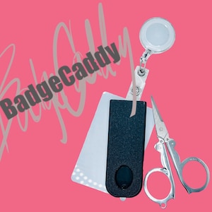 Könnte beinhalten: Ein schwarzer Badgehalter mit einer silbernen einziehbaren Badge-Rolle und einer kleinen silbernen Schere. Der Badgehalter hat eine strukturierte Oberfläche und der Text "BadgeCaddy" ist in Grau auf rosa Hintergrund geschrieben.