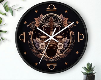 Puede incluir: Reloj de pared redondo negro con una esfera blanca y un diseño de símbolo del zodíaco de Libra en oro. El reloj tiene manecillas blancas y un marco negro.
