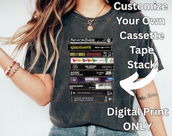 May include: Dark gray t-shirt featuring a stack of cassette tapes with band names like Guns N' Roses and AC/DC. The shirt has the text "Customize Your Own Cassette Tape Stack! Digital Print ONLY."