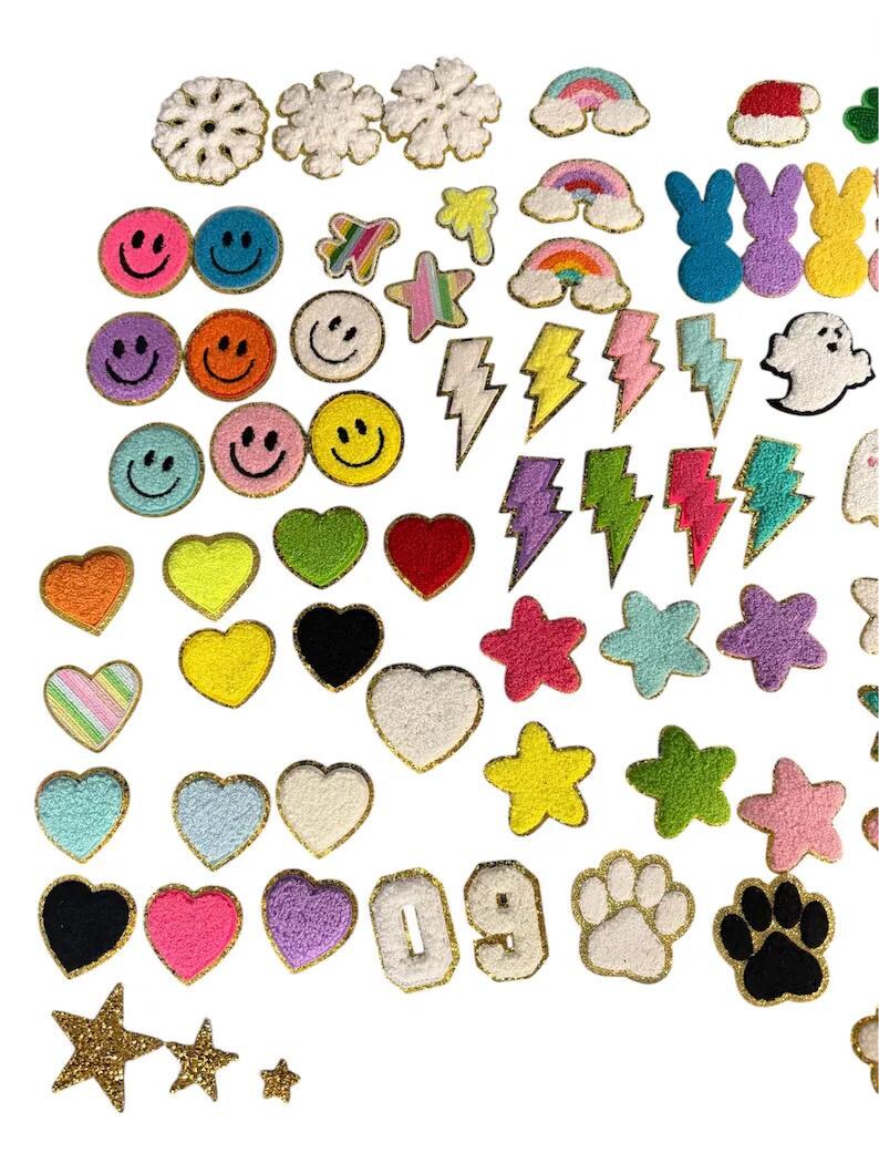 May include: A collection of assorted chenille patches featuring various shapes including smiley faces, hearts, stars, rainbows, lightning bolts, snowflakes, numbers 0 and 9, paw prints, and a ghost, all with gold-toned trim edges.