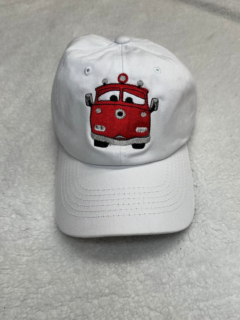 May include: White baseball cap with an embroidered red fire truck with a face on it.