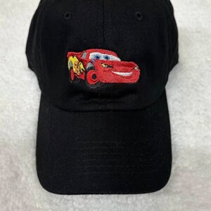 May include: Black baseball cap with an embroidered image of a red race car with a yellow lightning bolt on the side. The car has a smiling face.