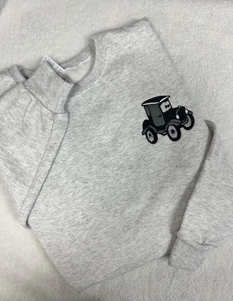 May include: A light gray sweatshirt with a crew neck and long sleeves. An embroidered black and gray vintage car is on the front. The sweatshirt is made of a soft, comfortable material.