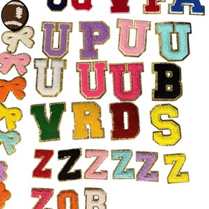 May include: A collection of embroidered iron-on patches featuring various letters of the alphabet in multiple colors with gold glitter borders, alongside patches shaped like a softball, a football, and several bows in different colors.