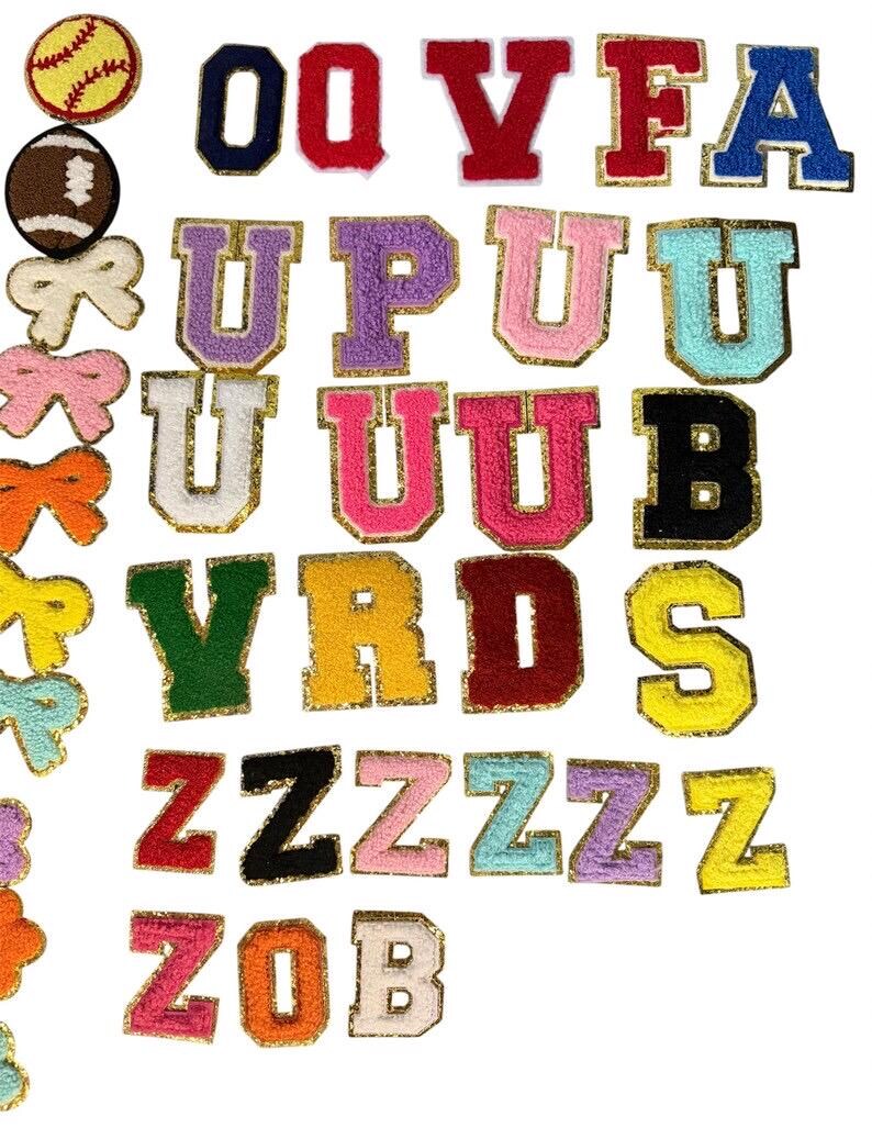 May include: A collection of embroidered iron-on patches featuring various letters of the alphabet in multiple colors with gold glitter borders, alongside patches shaped like a softball, a football, and several bows in different colors.