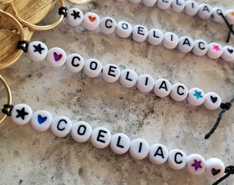 May include: Four keychains with black string and white beads spelling "COELIAC" with different colored hearts and stars on each bead.