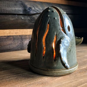 May include: A ceramic whale candle holder with a teal glaze and cut-out details. The candle holder is lit and casting a warm glow.