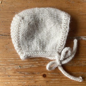 May include: A white knitted baby bonnet with a tie at the back.