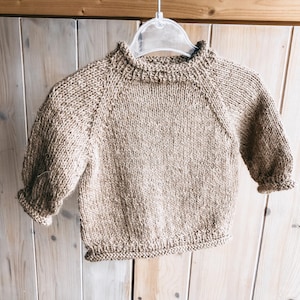 Op de afbeelding: Een bruine gebreide trui met een ronde hals en lange mouwen.