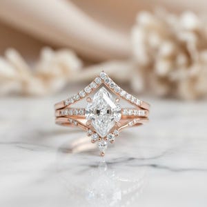 Peut inclure: Ensemble de bagues de fian&ccedil;ailles en or rose, comprenant une bague avec un diamant central de taille marquise. La bague est flanqu&eacute;e d'un anneau serti de diamants et d'un anneau en forme de chevron. Petits diamants suppl&eacute;mentaires.