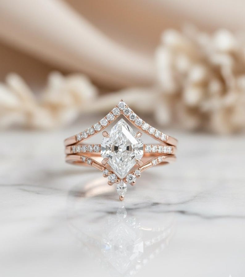 Peut inclure: Ensemble de bagues de fian&ccedil;ailles en or rose, comprenant une bague avec un diamant central de taille marquise. La bague est flanqu&eacute;e d'un anneau serti de diamants et d'un anneau en forme de chevron. Petits diamants suppl&eacute;mentaires.