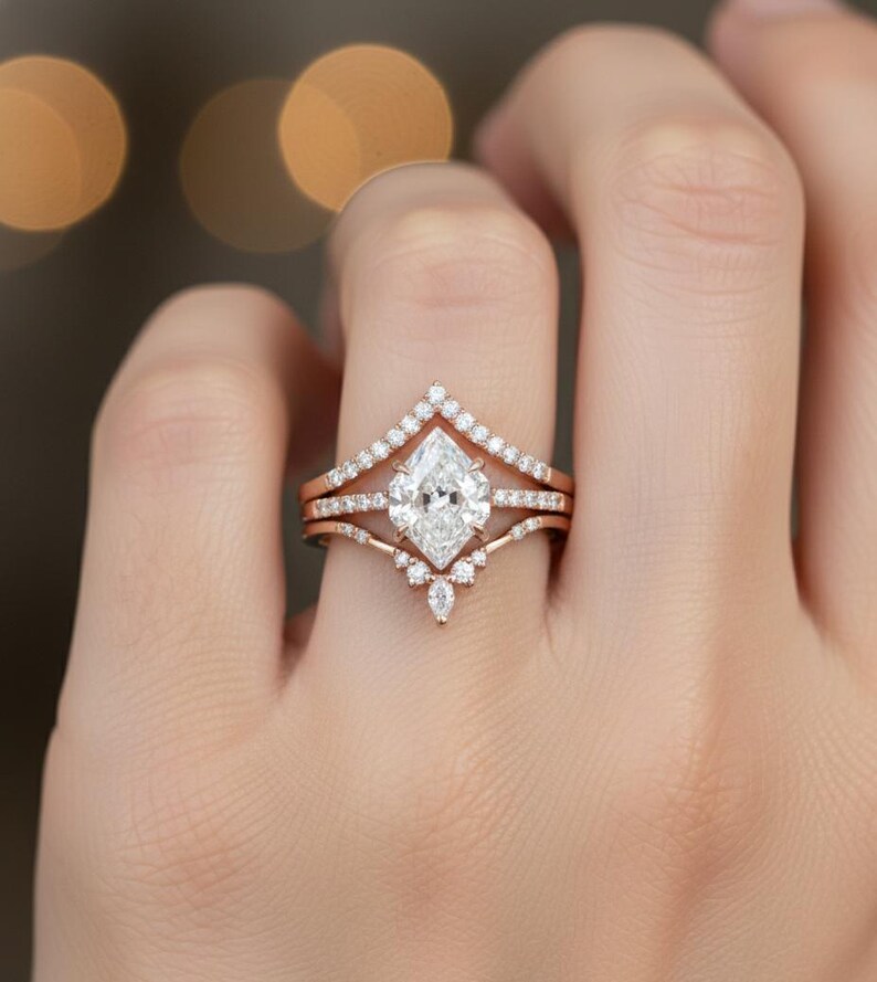 Peut inclure: Un ensemble de bagues de fian&ccedil;ailles en or rose, comprenant une bague principale avec un diamant central de taille marquise. L'ensemble comprend une alliance sertie de diamants et une bague en forme de chevron. Les bagues sont orn&eacute;es de petits diamants.