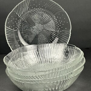 May include: A stack of clear glass bowls and a matching plate. The bowls have a textured, ridged design with small bubble-like details. The plate has a similar design with a central floral pattern.