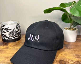 May include: A black baseball cap with a purple embroidered word "JOY" on the front.