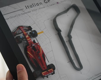 May include: Framed artwork featuring a red and black Formula 1 race car model, a track outline, and text that reads "Italian GP." The artwork is in a black frame and includes the text "Monza Circuit | 01 September 2024."