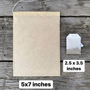 May include: A large, beige tea bag, measuring 5x7 inches, is displayed next to a smaller tea bag, 2.5 x 3.5 inches. Both bags have a string attached. The bags are on a weathered wooden surface.