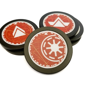 May include: A collection of black-rimmed game tokens with red and white graphics. The tokens feature geometric designs and symbols, including a white triangle and a starburst emblem. The tokens are stacked and scattered against a white background.