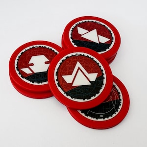 以下が含まれることがあります： 白と黒の幾何学模様が施された、赤い円形のゲームトークン。各トークンは、詳細なパターンを持つ赤い縁取りがあります。トークンは積み重ねられ、白い表面に散らばっています。