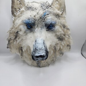 Peut inclure: Sculpture de tête de loup blanche avec des yeux bleus et un nez noir. La sculpture est faite d'un matériau texturé et a une apparence réaliste.
