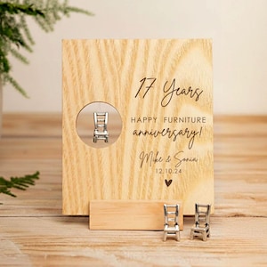 Può includere: Una targa di anniversario in legno con la scritta "17 Years Happy Furniture Anniversary!" e i nomi "Mike & Sonia". Un piccolo ciondolo a forma di sedia è visibile in un ritaglio circolare. Due ciondoli a forma di sedia in miniatura sono posti davanti alla targa.