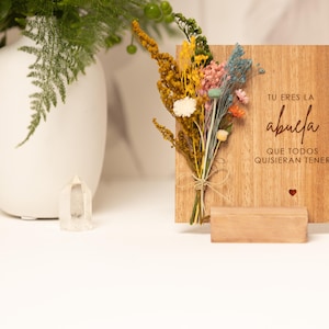 May include: A wooden sign with the text "Tu eres la abuela que todos quisieran tener" (You are the grandmother everyone would want to have) in red lettering. The sign is decorated with dried flowers and a small red heart.