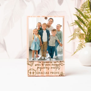 May include: Wooden photo frame with a picture of a teacher and students. The frame has a quote in Spanish that says "Se necesita un gran corazón para formar pequeñas mentes. Gracias profe." which translates to "It takes a big heart to shape young minds. Thank you teacher."