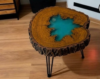 May include: A round side table featuring a natural wood slab top with a live edge and a central inlay of translucent turquoise resin. The table is supported by three thin black metal hairpin legs, showcasing the wood grain and bark.