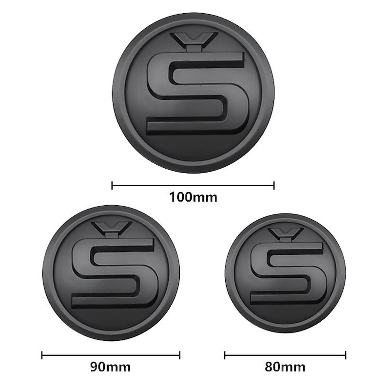 Może przedstawiać: Trzy czarne, okrągłe emblematy ze stylizowanym wzorem "S". Największy emblemat ma średnicę 100 mm, średni 90 mm, a najmniejszy 80 mm. Emblematy mają matowe wykończenie.