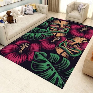 May include: A rectangular area rug featuring a dark background with a repeating pattern of large magenta hibiscus flowers, bright green monstera leaves, and tan tiki masks with green accents. The design covers the entire surface of the rug.