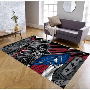 Puede incluir: Una alfombra de &aacute;rea colorida con una calavera con un sombrero y sosteniendo una grabadora. La calavera est&aacute; de pie frente a una bandera roja, blanca y azul con una estrella. La alfombra tiene un fondo gris con grafiti en blanco y negro.