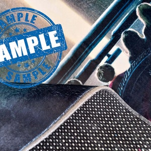 May include: A close-up of a blue and white rug with a black and white patterned backing. The rug has a frayed edge and a blue and white sample stamp.
