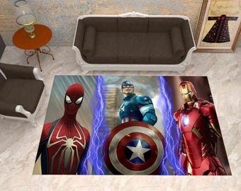 Puede incluir: Una alfombra rectangular con un estampado gráfico de tres superhéroes. A la izquierda, Spider-Man en rojo y azul; en el centro, el Capitán América con su escudo; y a la derecha, Iron Man en rojo y dorado, todos separados por rayos azules.