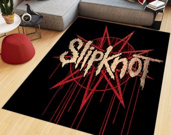 Könnte beinhalten: Ein rechteckiger Teppich mit schwarzem Hintergrund, einem großen roten Nonagramm-Sternsymbol und dem Wort Slipknot in einer abgenutzten, strukturierten beigen Schrift. Das Design enthält rote vertikale Linien, die an tropfende Farbe erinnern.