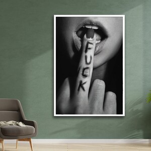 May include: Black and white photograph of a person's hand with the word "F.U.C.K." written on the index finger. The finger is placed in front of the person's mouth, which is slightly open.