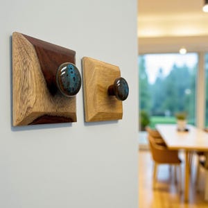 May include: Two wooden wall hooks. One hook features a square wooden base with a dark brown and light brown design, and a blue and brown ceramic knob. The other hook has a square light brown wooden base and a blue and brown ceramic knob.