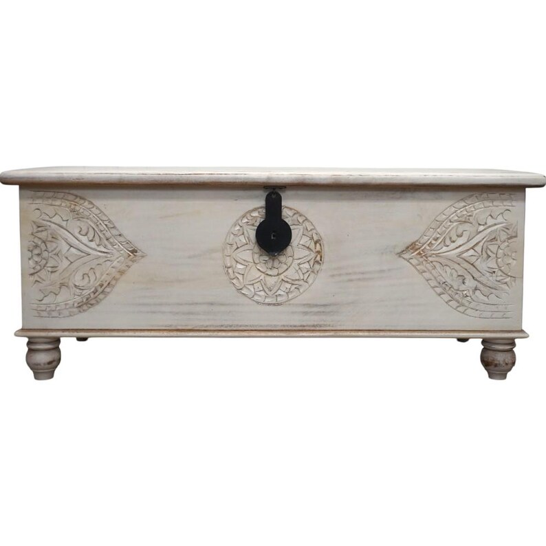 May include: White wooden storage chest with carved floral designs and a black metal latch. The chest has a distressed finish and sits on four turned legs.