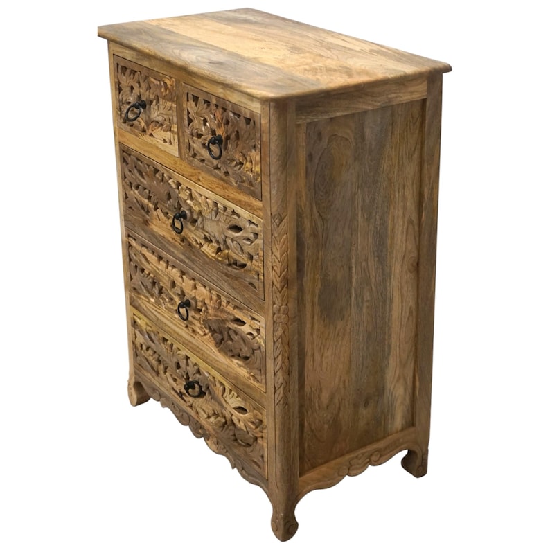 Op de afbeelding: Een houten ladekast met vijf laden en een bovenblad. De kast is gemaakt van lichtbruin hout met ingewikkelde bloemsnijwerken op de ladefronten. De laden hebben zwarte metalen ringtrekkers. De kast heeft een decoratief gesneden ontwerp aan de zijkant.