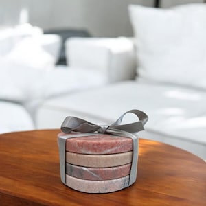 May include: Set of four pink and gray marble coasters tied together with a gray ribbon. The coasters are round and have a natural, polished finish.