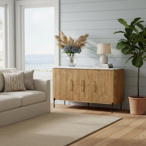 K&ouml;nnte beinhalten: Ein helles Holzschrank mit einer wei&szlig;en Marmorplatte, drei T&uuml;ren und schwarzen Beinen. Der Schrank befindet sich in einem Wohnzimmer mit einem beigen Teppich, einem Sofa und einem gro&szlig;en Fenster mit Blick auf das Meer. Eine Lampe und eine Blumenvase stehen oben.