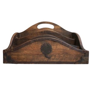 May include: A vintage wooden desk organizer with a handle and multiple compartments. The organizer is made of dark wood and features a decorative metal emblem. The corners are reinforced with metal. A practical and stylish storage solution.